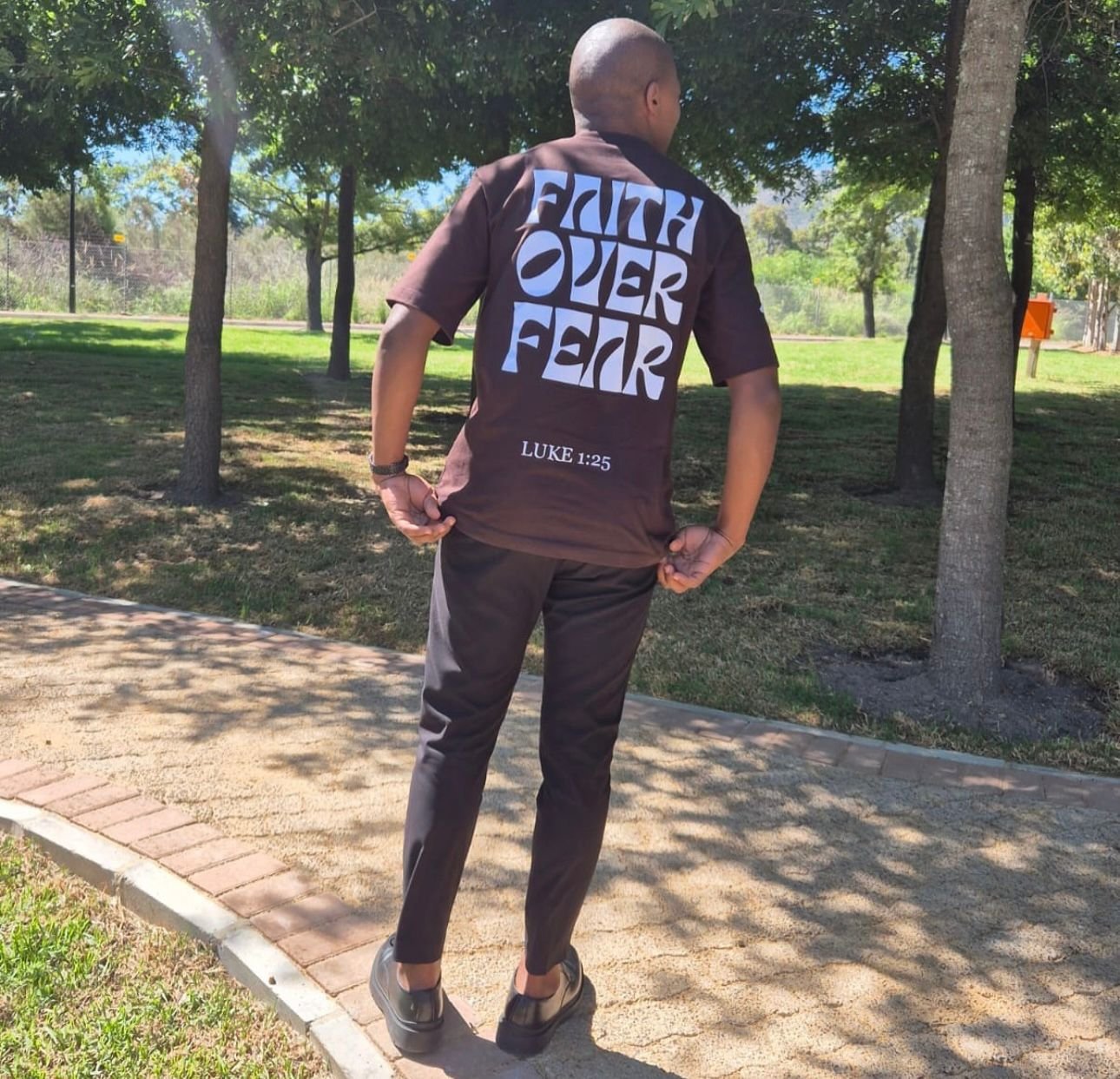 Faith Over Fear tee in chocolate brown, worn in a sunlit park