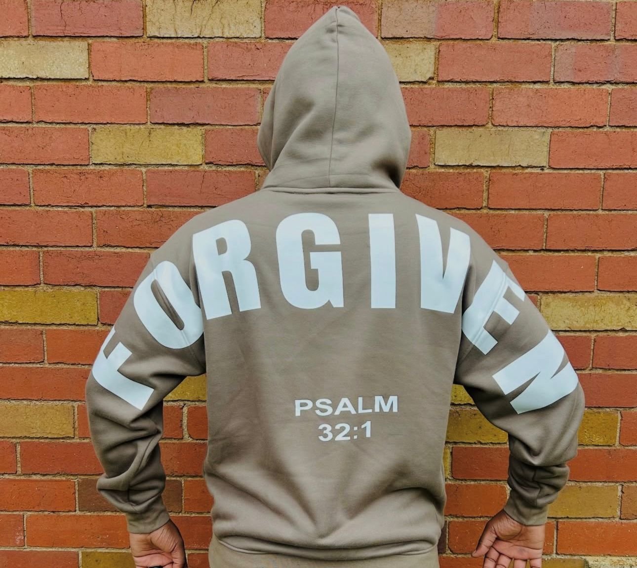 FORGIVEN hoodie — Psalm 32:1 — against a brick wall